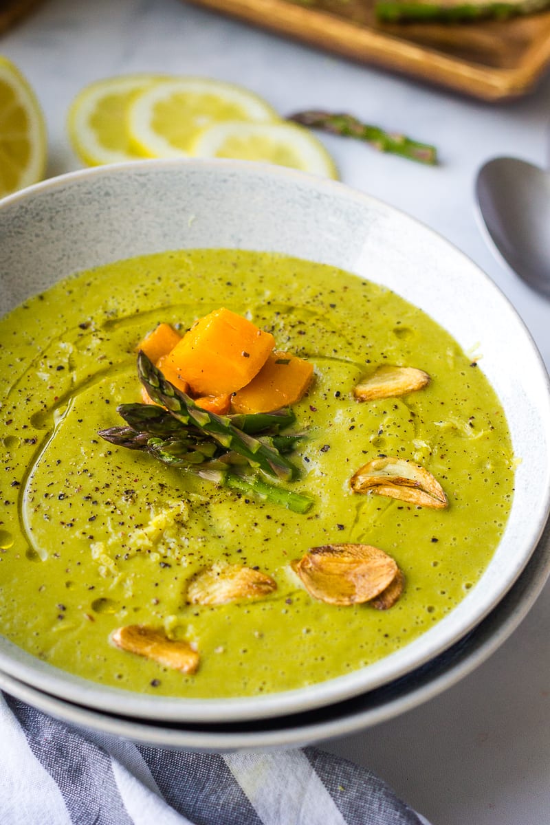 vegan asparagus soup in a bowl topped with garlic chips, and butternut squash