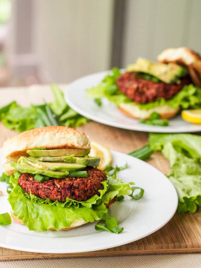 Beet veggie burger sandwiched between bread roll with lots of avocado
