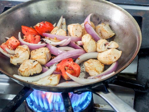 chicken stir fry in the pan with red onions and tomatoes