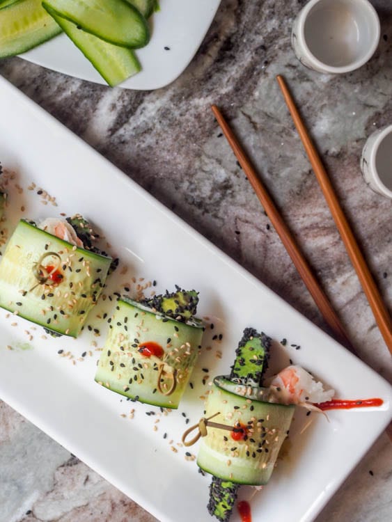 three avocado cucumber rolls on a serving dish with chopsticks