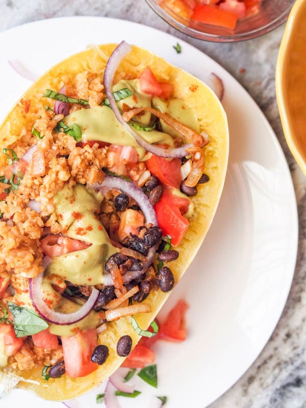 stuffed spaghetti squash taco bowls with vegan taco meat, beans, red onions, tomatoes and an avocado sauce