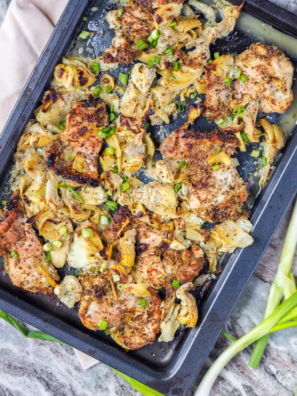 broiled chicken thighs with artichoke hearts, garlic and oregano on a baking tray 