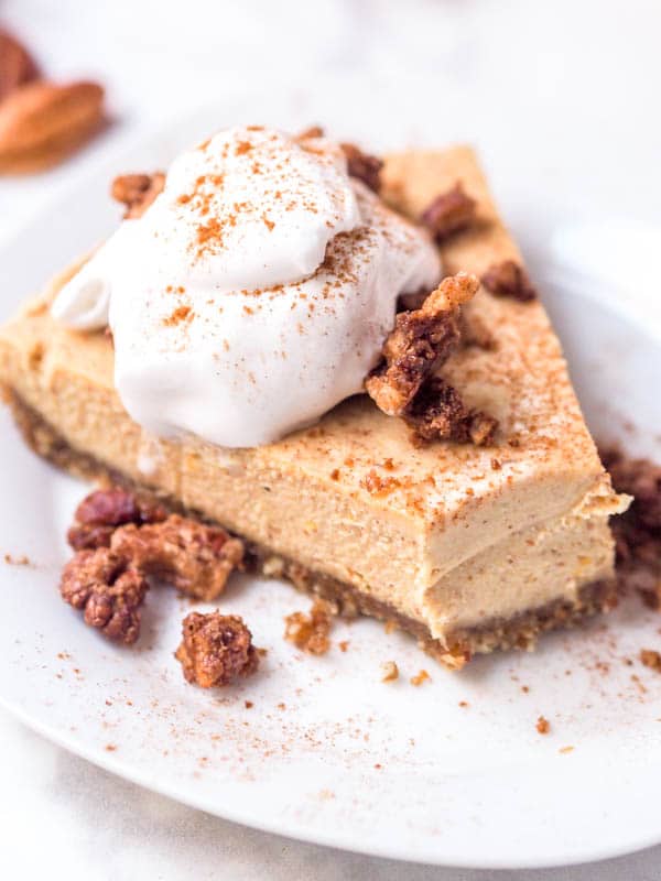 Plated slice of vegan pumpkin cheesecake with whipped coconut cream and pecans