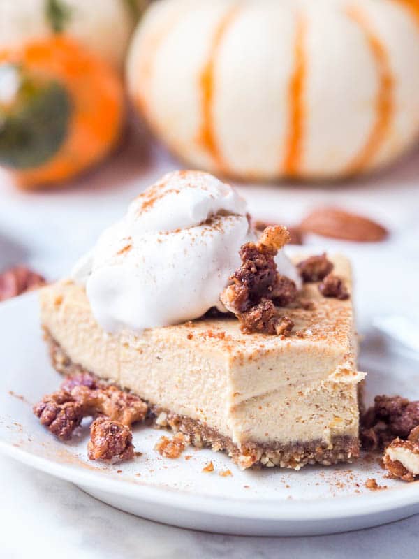 slice of vegan pumpkin cheesecake with a dollop of coconut cream and candied pecans