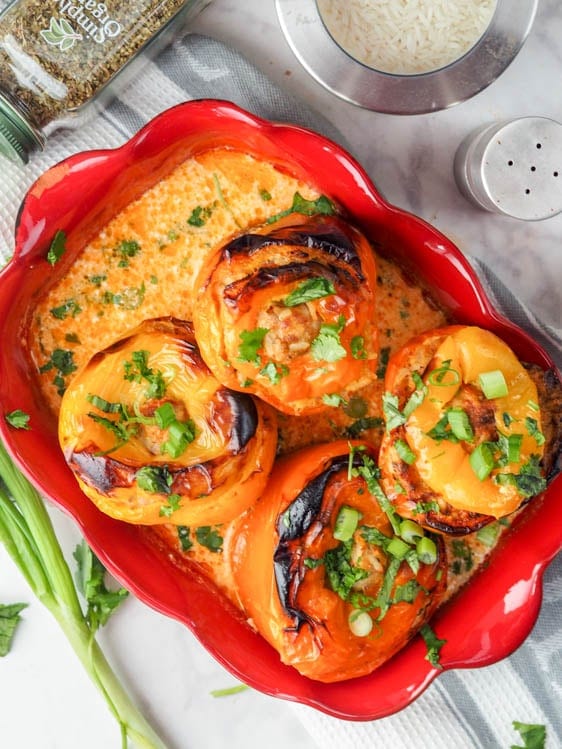 chicken stuffed peppers with rice and carrots in a red casserole dish