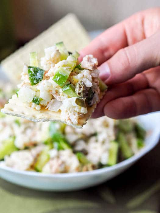 taking a bite out of tuna egg salad made with rice, capers, cucumbers and mayo served on crackers